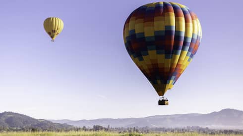 Close-up of a multi-coloured hot-air balloon close to the ground; a second yellow and red balloon floats higher above it.