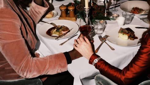 Two guests sitting at a dining table holding hands and a glass of wine.