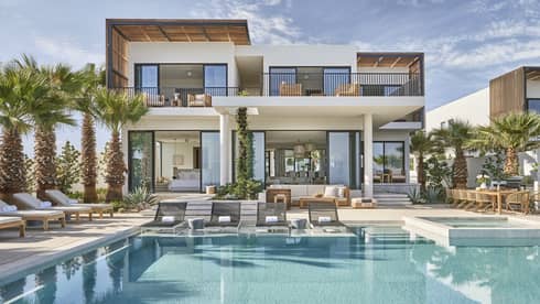 Modern luxury villa with a spacious pool area, surrounded by palm trees, featuring outdoor lounge chairs, a dining area, and floor-to-ceiling windows.