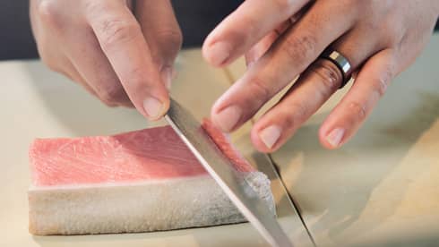 Person cutting a pink piece of food on a counter into slices