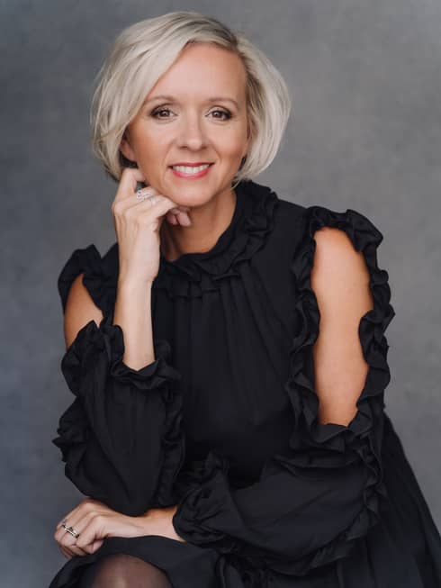 Marta Hobbs in black dress, leaning with elbow onto knee and smiling