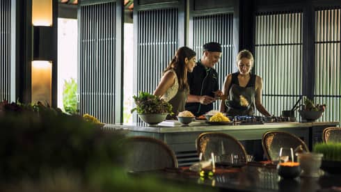 Chef, two women look at pan on kitchen range at Hoi An Cooking Academy 
