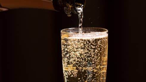 A bottle of champagne is poured into a glass as bubbles float to the top