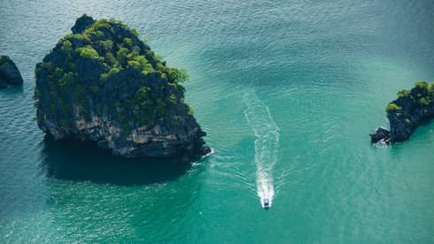 Ariel view of a boat driving through rock structures on emerald green water 