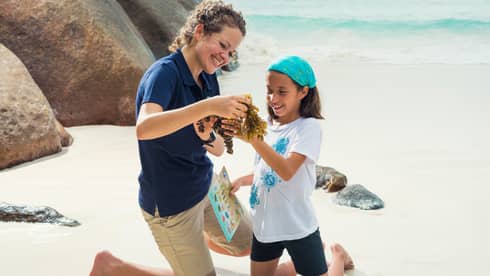 A WiseOceans female employee teaches a young girl about ecology on a beach