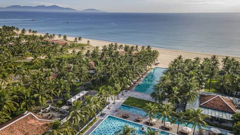 Aerial view of the resort pools with ocean views, palm trees and blue skies