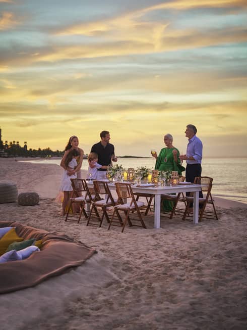 Family standing around dining table on the beach.