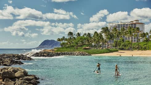 Two people on stand-up paddleboards in lagoon with beach and resort in background