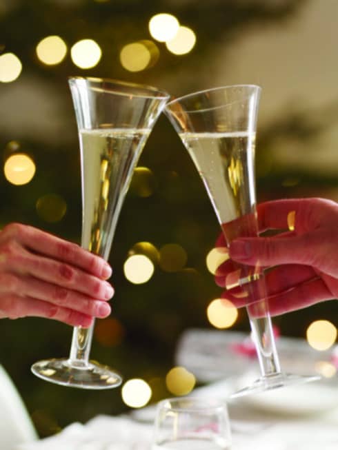 Close-up of long Champagne glasses in toast, festive gold lights in background