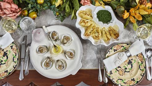 Many food dishes including clams and a salad bowl along with a table centrepiece.