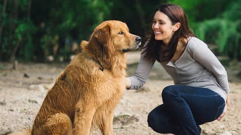 A woman petting a dog outside at a park trail.