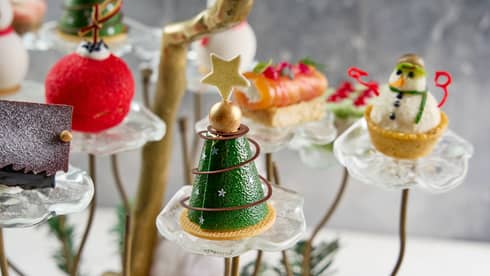 Holiday pastries shapped like a  Christmas tree, snowman, red ball ornament and small house are on display on small glass pedastals
