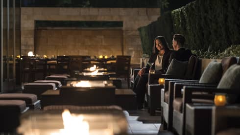 Two people in business attire sit in candle-lit cocktail lounge chairs with martinis