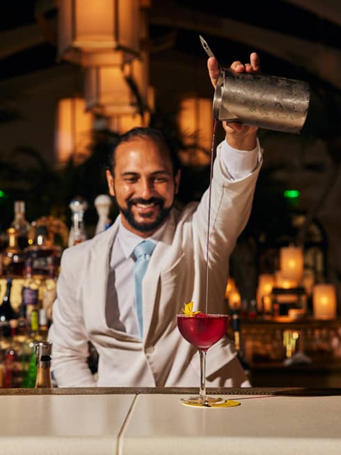 Bartender pours a cocktail from a silver cocktail shaker into a glass