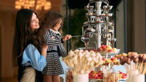 Adult lifts a small child up to grab a pastry from a buffet display