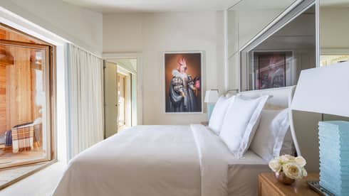 Side view of white-dressed bed, blue lamp beside, portrait on wall at end