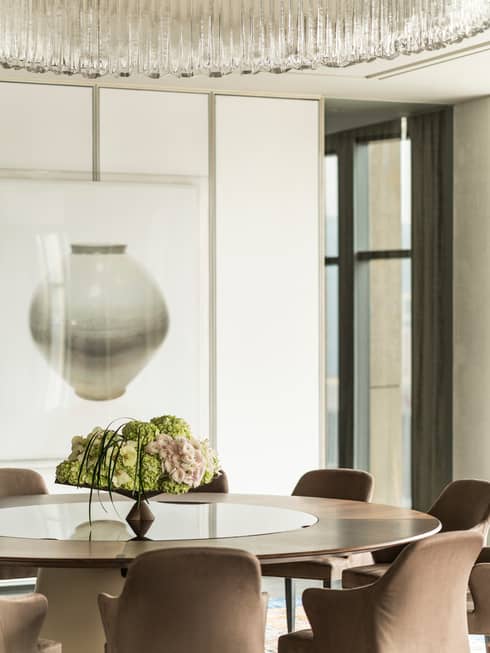 Floral display in vase on round table with upholstered chairs under modern, round crystal chandelier