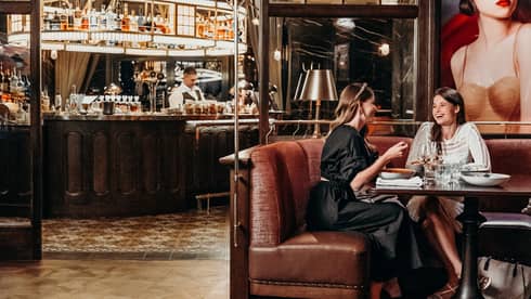 Two women sit on leather booth in restaurant