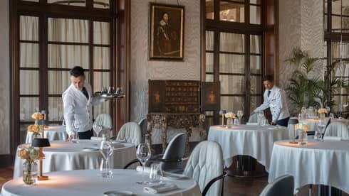 Two male servers in white jackets set dining tables in restaurant