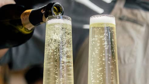Person wearing an apron and pouring champagne into two glasses