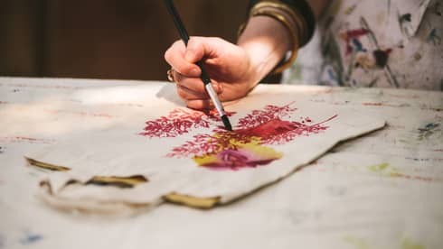 Close-up of woman with paint brushes painting flowers on canvas bag
