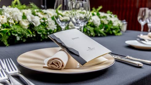 A wedding dinner table showcasing a crisp rolled napkin, elegant cutlery, floral arrangements and a stylish small booklet.