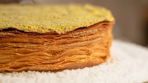 Close up of multi-layered pastry cake surrounded by white powdered sugar on a glass cakestand