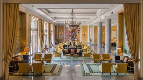 Bright hotel lobby with long gold curtains and armchairs, seating area under chandelier