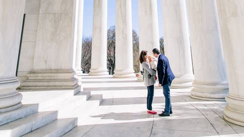 Candid portrait of mother, father, and baby in front of the large white columns of the capitol building