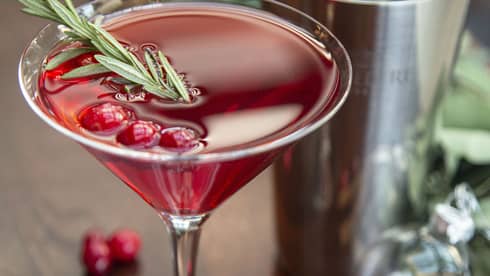 Berry Merry Martini, a red cocktail with rosemary sprig and cranberries