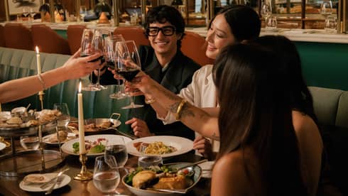 A group clinks glasses of red wine over a dining table filled with various vibrant culinary dishes