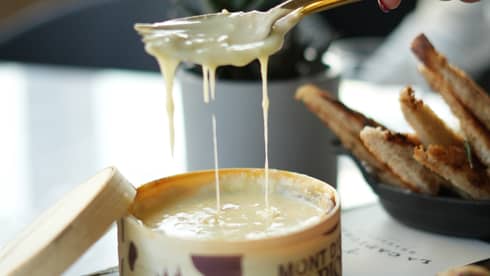 Hand holding a spoon and fork scoops out a serving of melted cheese
