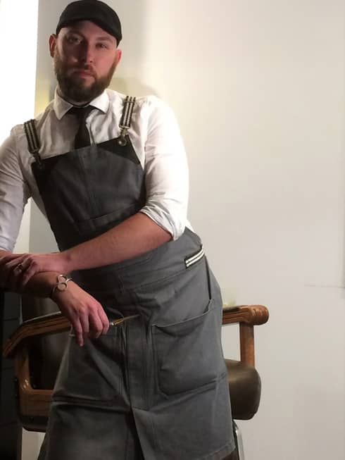 A portrait of bartender Guy Bruha leaning against a bar stool and looking at the camera with a stoic face