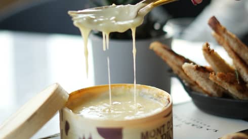Hand holding a spoon and fork scoops out a serving of melted cheese