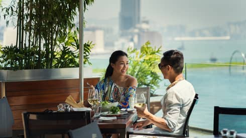 Two people smiling, dining at sunny Poolside Terrace patio table