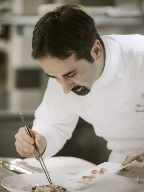 Executive Chef Vito Mollica in white uniform, picks up small shrimp with kitchen tweezers