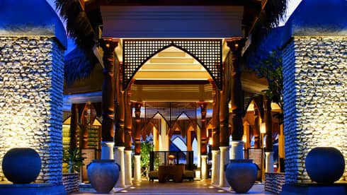 Outdoor entrance to restaurant, with illuminated steps, blue sky at desk, two planters