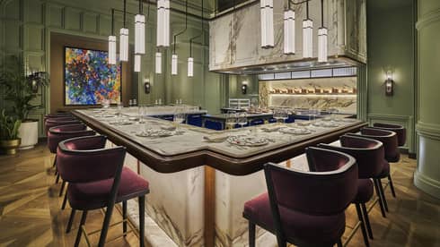 Marble counter with red chairs surrounds an open kitchen with green walls all around