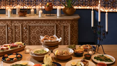 A table set with a variety of appetizers on white plates and bowls with a sideboard in the background adorned with white pillar candles