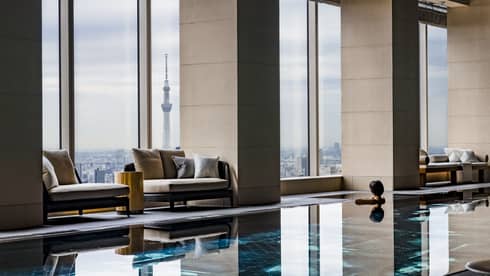 Four Seasons indoor pool with city skyline view through large windows, featuring comfortable seating and a prominent tower in the distance
