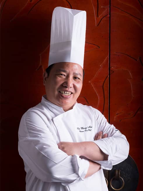 Portrait of Yu Yue Heen Executive Chef Mai Zhi Xiong in white chef's coat and hat