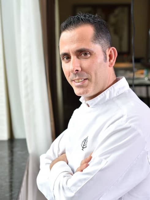 Portrait photo of Quadrum Chef Elias Caschili in white chef's jacket, arms crossed