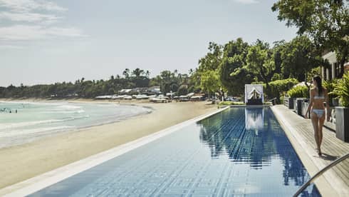 Woman in bikini walks by long Sundara infinity swimming pool over white sand beach