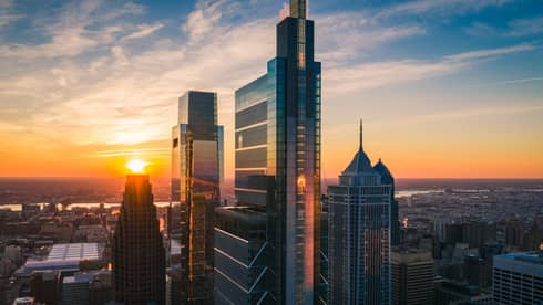 Philadelphia’s skyscrapers soaring above an expansive city, with a sunset-illuminated sky in the background.