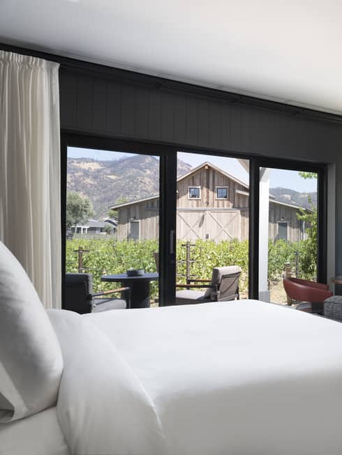 Luxury resort room with a king bed, cozy fireplace, vineyard view, seating area and outdoor patio facing rustic barn and mountains