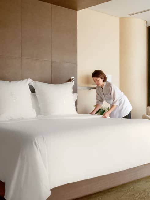 Hotel staff making a Four Seasons bed with white linens in a hotel room