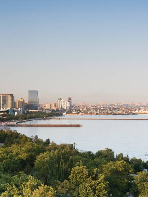 Aerial view of Baku skyline during the day with canopy of trees, high rise buildings, Caspian Sea