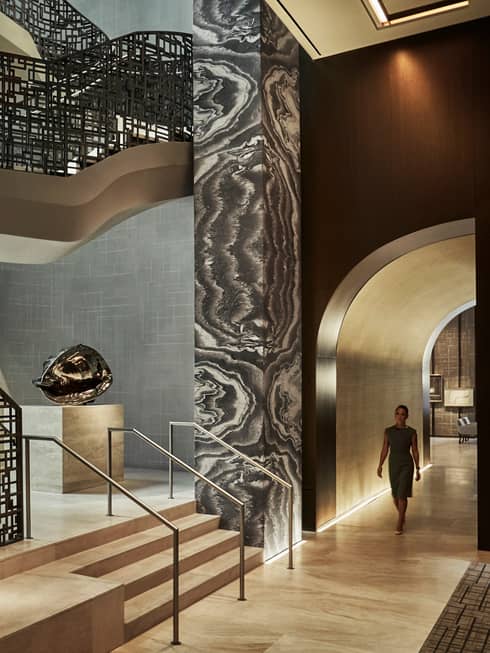 Woman walks down hall past tall black-and-white pillar, modern silver sculpture, black railings