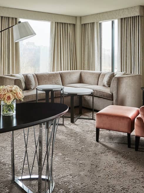 Capital Suite living room with long oval work desk in front of L-shaped sofa, pink armchair, corner windows
