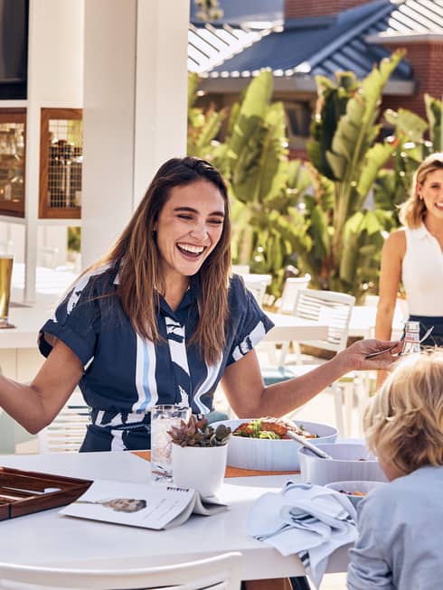 Woman and child laughing at table while sharing a meal.